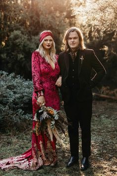 a man and woman standing next to each other in front of some trees with flowers