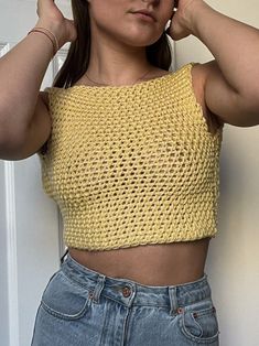 a woman wearing a yellow crop top and denim shorts with her hands on her head