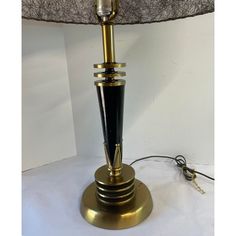 a black and gold table lamp with a white shade on the top, next to a corded light