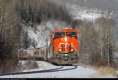 an orange train traveling down tracks next to snow covered trees