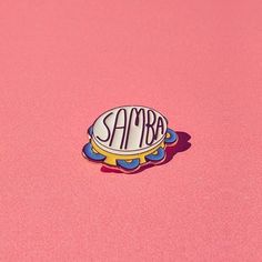 a pin with the word samba on it sitting on a pink surface in front of a white background