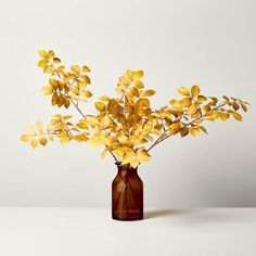 a brown vase filled with yellow flowers on top of a white table next to a wall