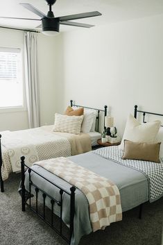 two beds in a bedroom with white walls and carpeted flooring, one has a checkered blanket on it