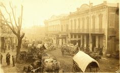 an old photo of horses and carriages on a street with people standing in the background