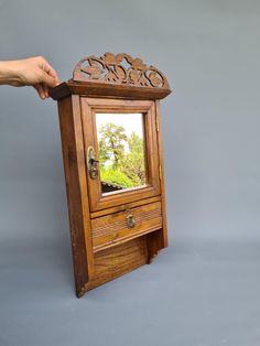 a hand holding a mirror on top of a wooden cabinet