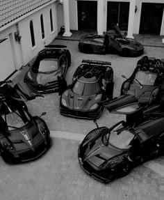 black and white photograph of four supercars parked in front of a house