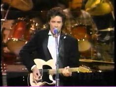 a man in a tuxedo singing into a microphone and playing an electric guitar