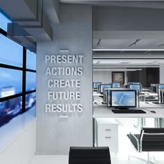 an office filled with computer monitors and desks next to a wall that says present actions create future results