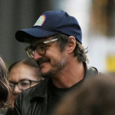 a man with glasses and a hat is smiling for the camera while people look on