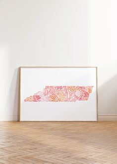 an art print is hanging on the wall next to a wooden floor in front of a white wall