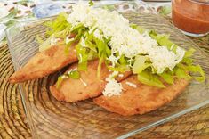 two fish fillets with lettuce and cheese on a glass plate next to sauce