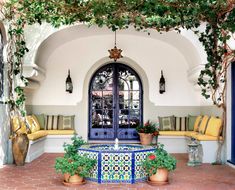 an outdoor area with potted plants, benches and a fountain in front of the door