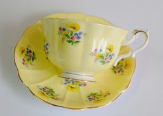 a yellow tea cup and saucer with flowers on it, against a white background