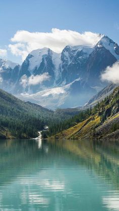 the mountains are covered in snow and clouds above water with trees on both sides of it