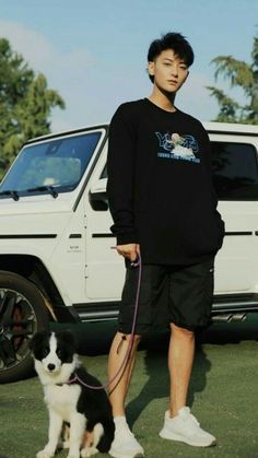 a man standing next to a black and white dog on a leash near a car