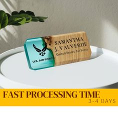 a wooden business card holder sitting on top of a white table next to a plant