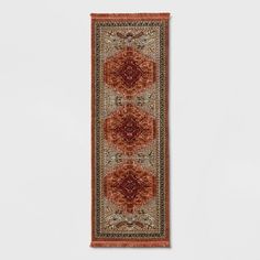 an orange and red rug hanging on the wall with white walls in the back ground