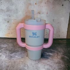 a pink and gray coffee cup sitting on top of a cement floor next to a wall