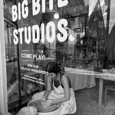 a woman sitting in front of a store window making clay pots with her hands on the ground