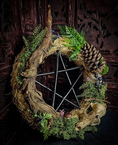 a wreath made out of branches and pine cones on a black surface with other greenery around it