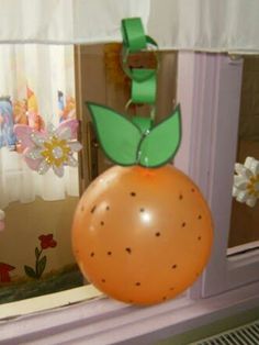 an orange balloon with a green leaf on it sitting in front of a window sill