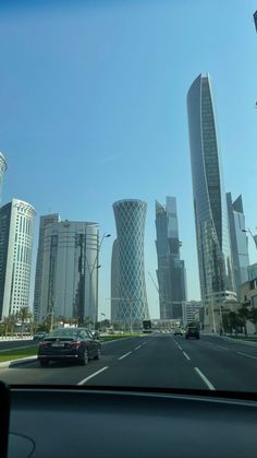 cars driving down the road in front of tall buildings with skyscrapers on either side