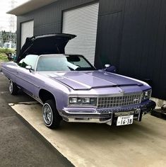 a purple car is parked in front of a garage with its hood open and it's trunk opened