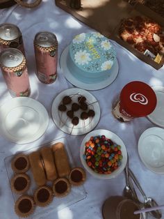 a table topped with lots of different types of food next to cans of sodas