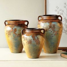 three vases sitting on top of a table next to a framed photo and books