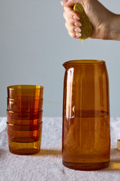 a person is pouring liquid into a pitcher and two glasses on a table with white linen