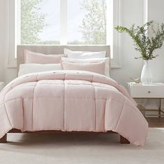 a bed with pink comforter and pillows in front of a window