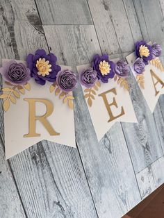 purple and gold paper flowers are hanging from a banner