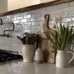 white tulips are in vases on the kitchen counter next to a cutting board