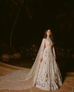 a woman in a wedding dress standing on a patio at night with palm trees behind her