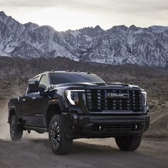 a black truck driving down a dirt road in front of snow covered mountain range with mountains