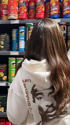 a woman with long hair wearing a white hoodie in front of shelves of canned food