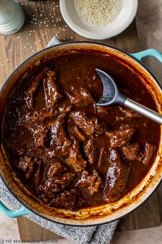 a pot filled with beef and brown sauce on top of a wooden table next to other dishes