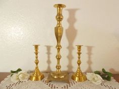 three gold candlesticks and two white roses on a doily