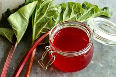 a glass jar filled with red liquid next to some green leafy vegetables on a table