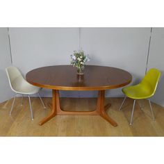 a wooden table with two chairs and a vase on the top, in front of a white wall