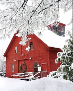 a red barn with snow on the ground and trees in front of it, during winter