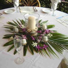 an arrangement of flowers, candles and wine glasses on a table with white linens