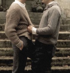 two men standing next to each other in front of some steps and stairs with their hands together