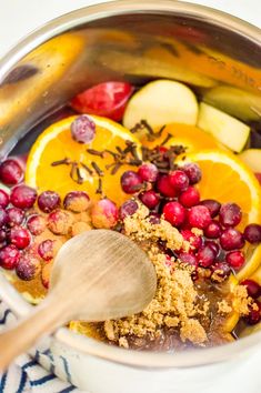 a bowl filled with cranberries, oranges and other food items next to a wooden spoon