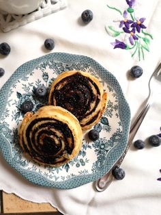 two pastries on a plate with blueberries next to some silverware and flowers