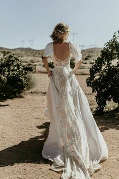 a woman standing in the desert wearing a white dress with an open back and short sleeves