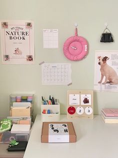 a white desk topped with lots of books and office supplies next to a pink clock