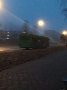 a green bus driving down a street next to a sidewalk with lights on at night