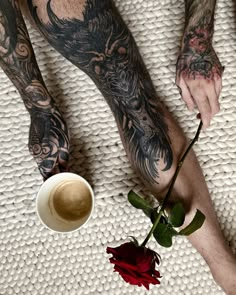 a man with tattoos on his arms and legs holding a rose next to a coffee cup