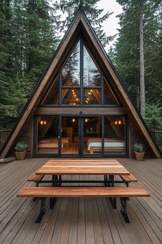 a - frame cabin in the woods with picnic table and large windows on deck area